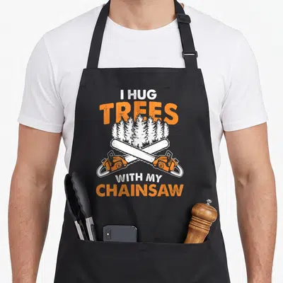Tablier de cuisine noir avec inscription I hug trees with my chainsaw et deux tronçonneuses croisées sur fond de forêt.