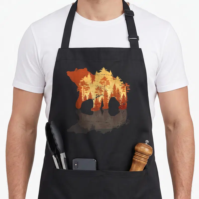 Tablier de cuisine noir avec silhouette d'ours grizzly et motifs de forêt orange et jaune