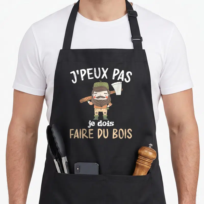 Tablier de cuisine noir avec personnage de bûcheron moustachu tenant une scie et le texte J'peux pas je dois faire du bois.