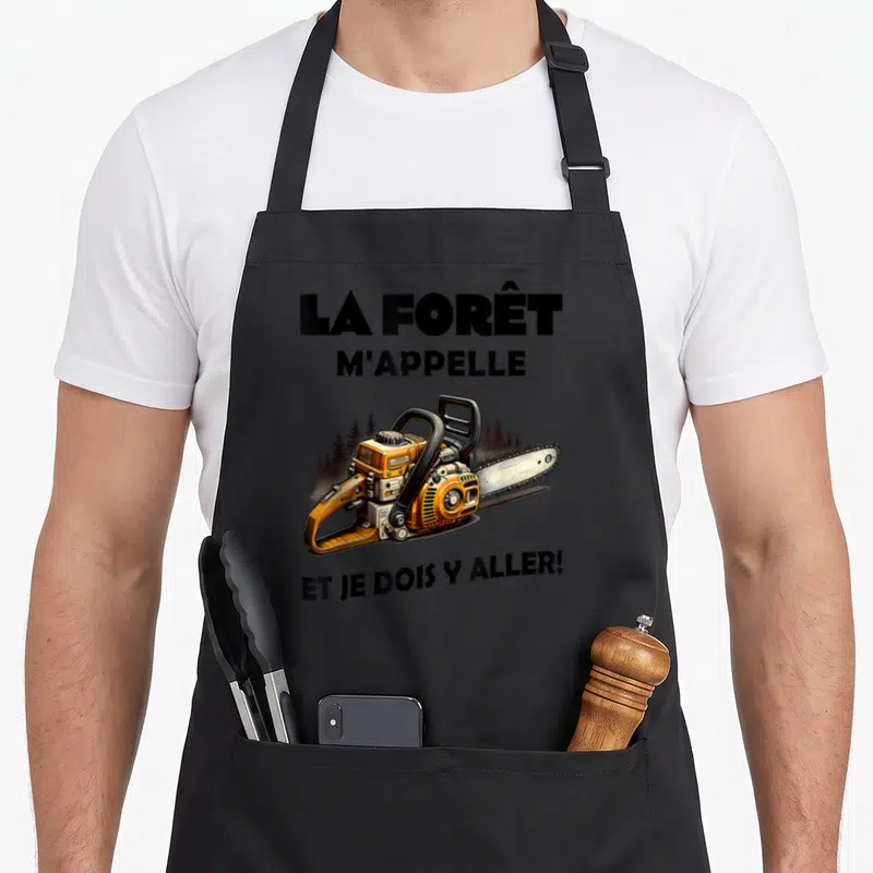Tablier de cuisine noir avec illustration de tronçonneuse orange et texte la forêt m'appelle et je dois y aller.