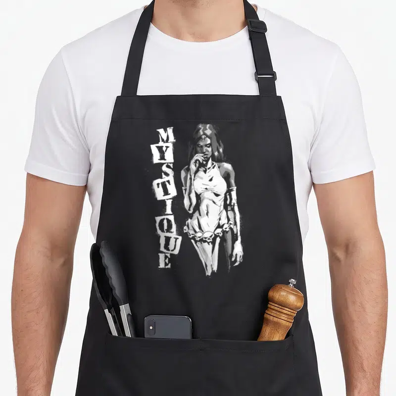 Tablier de cuisine noir avec illustration grise de Mystique et texte vertical blanc MYSTIQUE sur le côté gauche.