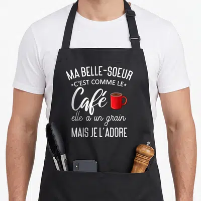 Tablier de cuisine noir avec texte blanc Ma belle-sœur c'est comme le café et une illustration de mug rouge vif.