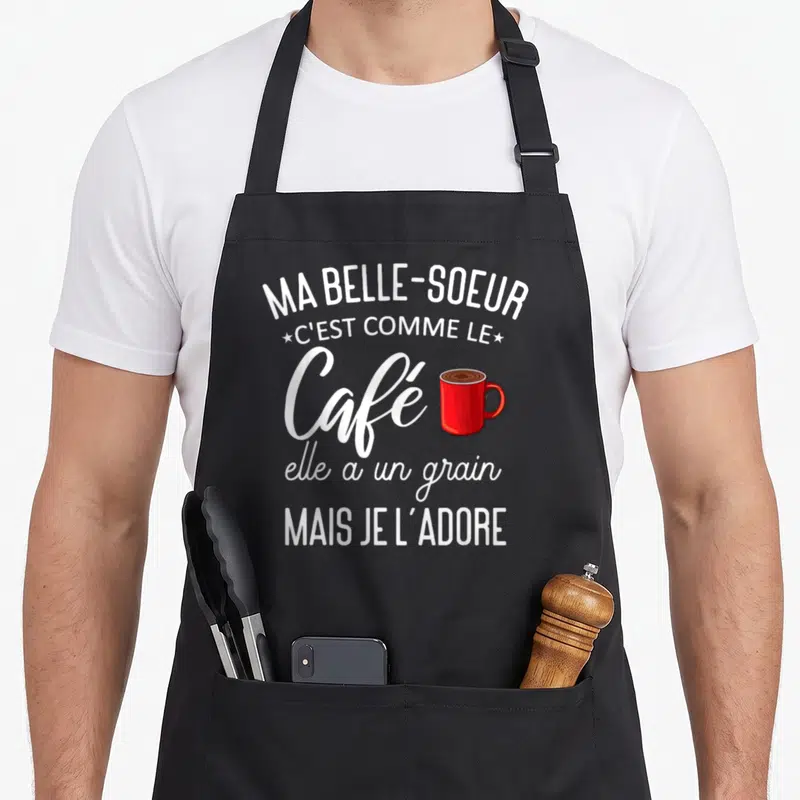 Tablier de cuisine noir avec texte blanc Ma belle-sœur c'est comme le café et une illustration de mug rouge vif.