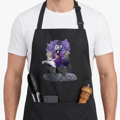 Tablier de cuisine noir avec Jack Skellington, son chien fantôme Zero et des tombes gravées R.I.P sous un ciel violet.
