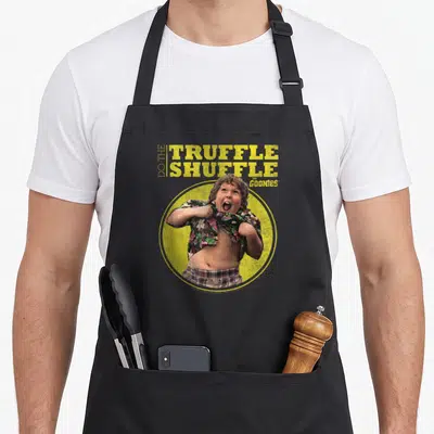 Tablier de cuisine noir avec illustration de Chunk et texte Do The Truffle Shuffle The Goonies sur fond jaune.