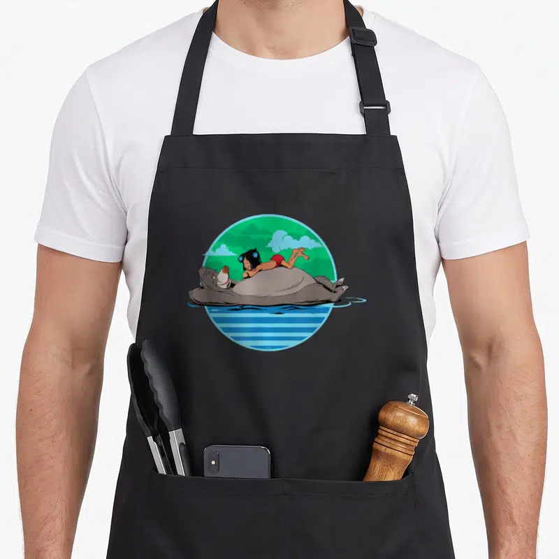 Tablier de cuisine noir avec illustration circulaire de Baloo et Mowgli flottant sur l'eau verte et bleue.