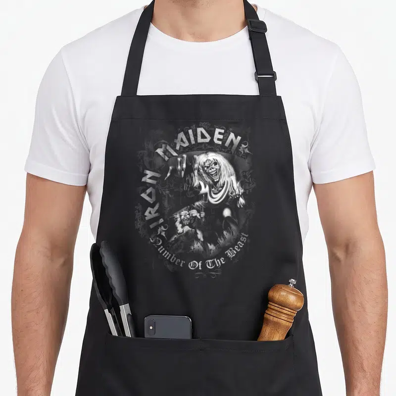 Tablier de cuisine noir avec illustration monochrome d'Eddie tenant une fourche sous le logo Iron Maiden.