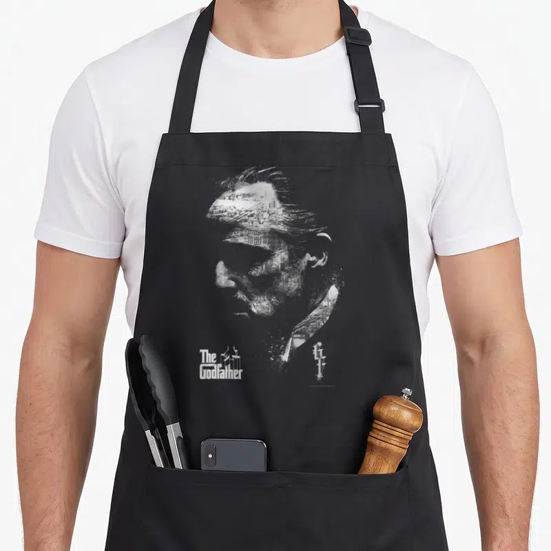 Tablier de cuisine noir avec portrait de profil de Don Vito Corleone et logo The Godfather en blanc.