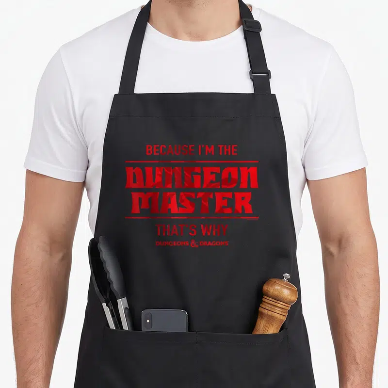 Tablier de cuisine noir avec inscription rouge Because I'm The Dungeon Master That's Why et logo Dungeons Dragons en bas.