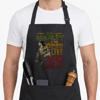 Tablier de cuisine noir avec illustration vintage de Bob Marley et le texte Rastaman Vibration Tour London 1976 imprimé au centre.