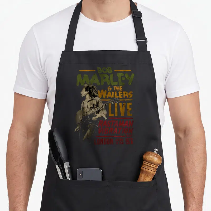 Tablier de cuisine noir avec illustration vintage de Bob Marley et le texte Rastaman Vibration Tour London 1976 imprimé au centre.
