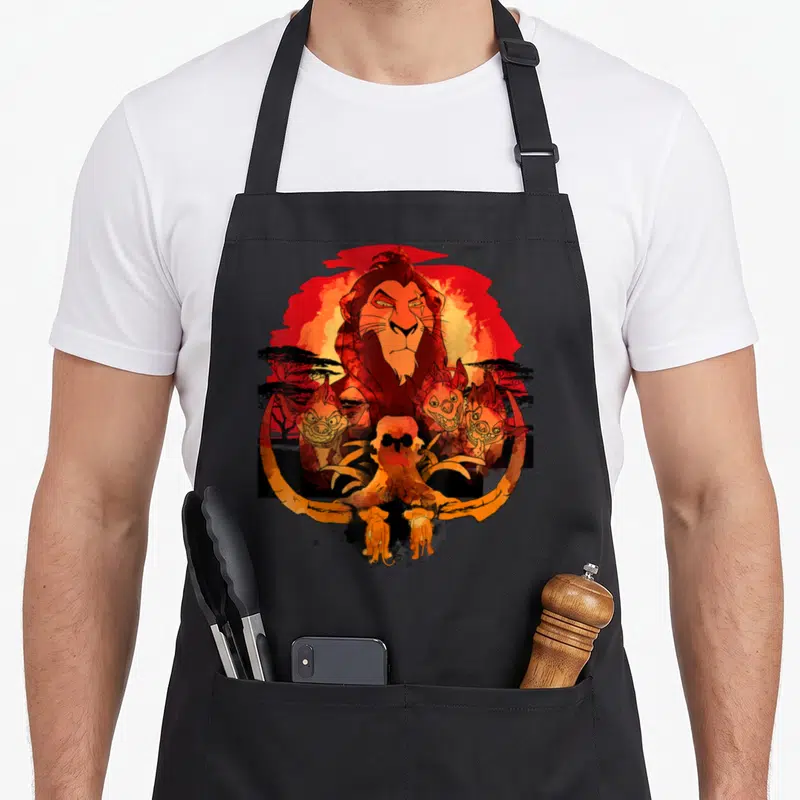 Tablier de cuisine noir avec illustration colorée de Scar, Simba, Nala et des hyènes devant un ciel rougeoyant.