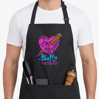 Tablier de cuisine noir avec un cœur rose traversé par un pieu et le logo bleu de la série.