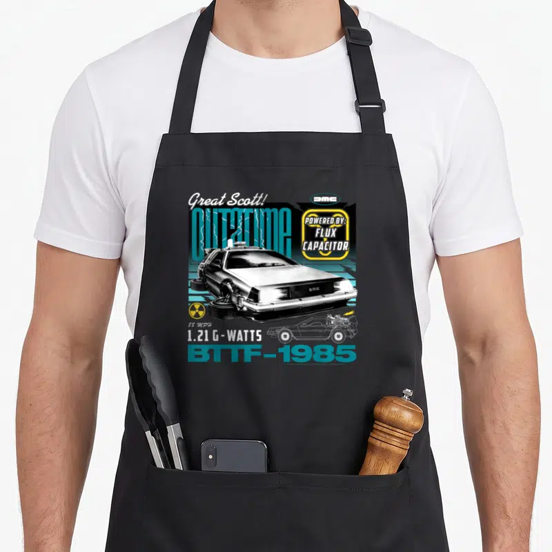 Tablier de cuisine noir avec illustration DeLorean, texte « Great Scott » et logo « Flux Capacitor » jaune et bleu turquoise.