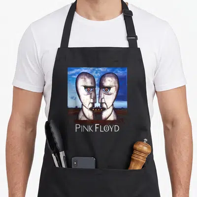 Tablier de cuisine noir avec deux têtes métalliques et le texte Pink Floyd imprimé au centre.