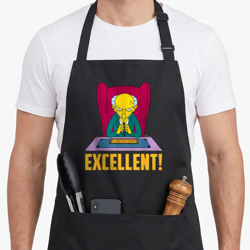 Tablier de cuisine noir avec Mr. Burns assis à son bureau et le mot Excellent en lettres jaunes.
