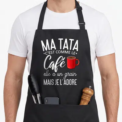 Tablier de cuisine noir avec texte blanc Ma tata c'est comme le café et illustration d'un mug rouge vif au centre du design imprimé.