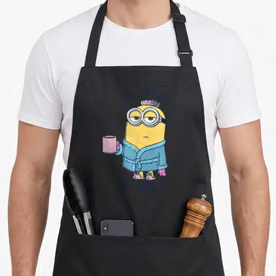 Tablier de cuisine noir avec le Minion Dave en peignoir tenant une tasse rose fumante.
