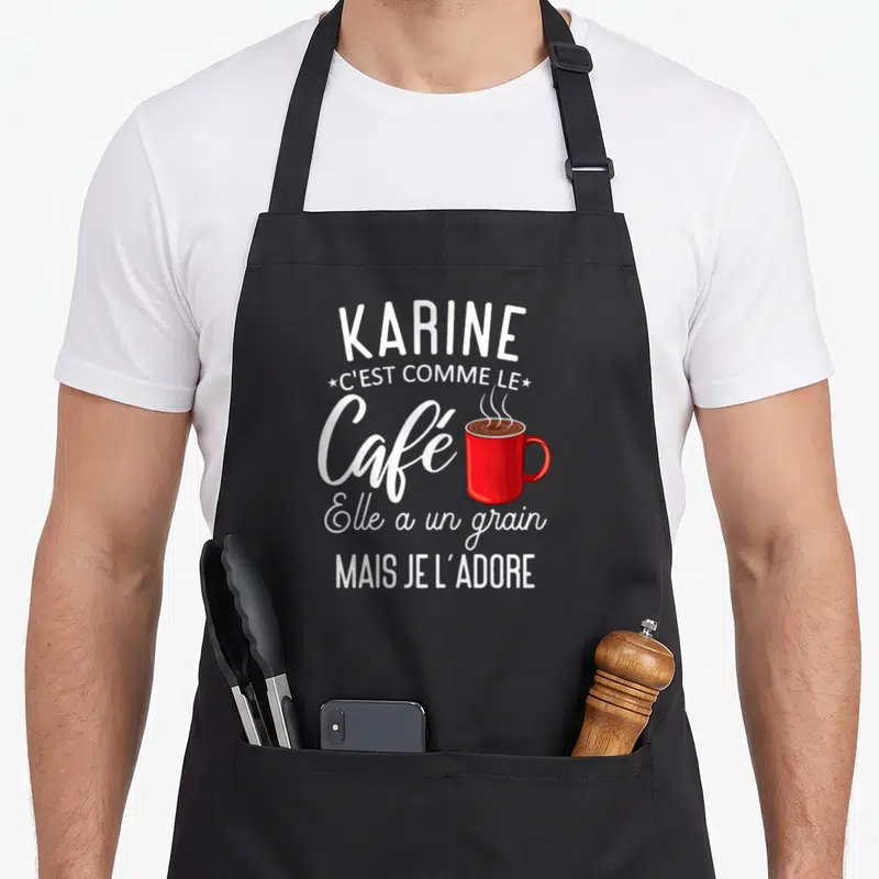 Tablier de cuisine noir avec inscription blanche Karine et illustration de tasse de café rouge fumante au centre du motif imprimé.