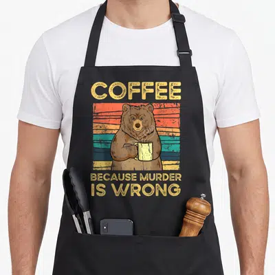Tablier de cuisine noir avec un ours tenant une tasse et le texte Coffee Because Murder Is Wrong vintage en jaune.