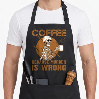 Tablier de cuisine noir avec un squelette tenant une tasse de café et du texte orange en anglais.