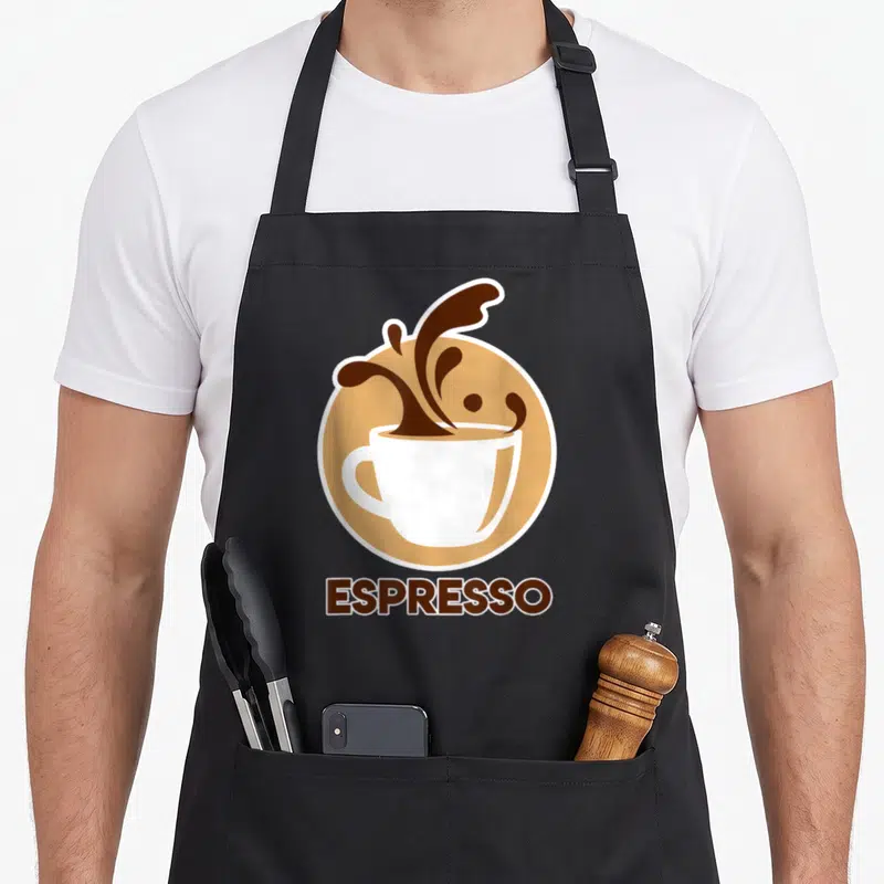 Tablier de cuisine noir avec une tasse blanche et des éclaboussures brunes sur fond rond beige, le mot Espresso en bas.