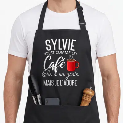 Tablier de cuisine noir avec inscription blanche Sylvie et illustration d'une tasse de café rouge fumante.