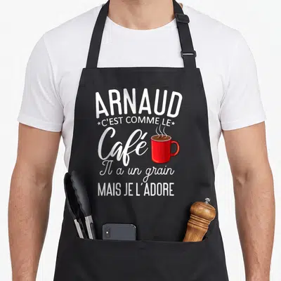 Tablier de cuisine noir avec inscription blanche Arnaud c'est comme le café et illustration d'une tasse rouge fumante au centre du motif.