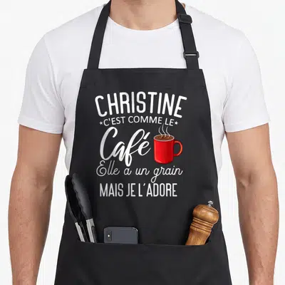 Tablier de cuisine noir avec inscription blanche Christine c'est comme le café et illustration de mug rouge fumant au centre.