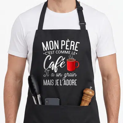 Tablier de cuisine noir avec inscription blanche et illustration de tasse de café rouge fumante au centre du motif.