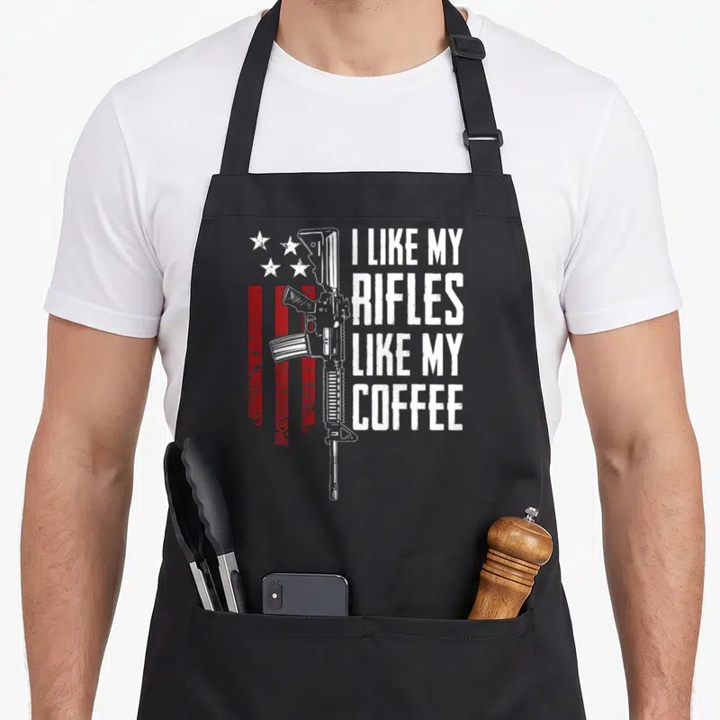 Tablier de cuisine noir avec inscription I Like My Rifles Like My Coffee et dessin de fusil sur fond de drapeau rouge et blanc.