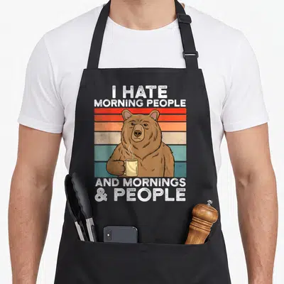 Tablier de cuisine noir avec ours tenant une tasse et texte blanc sur bandes colorées rétro.