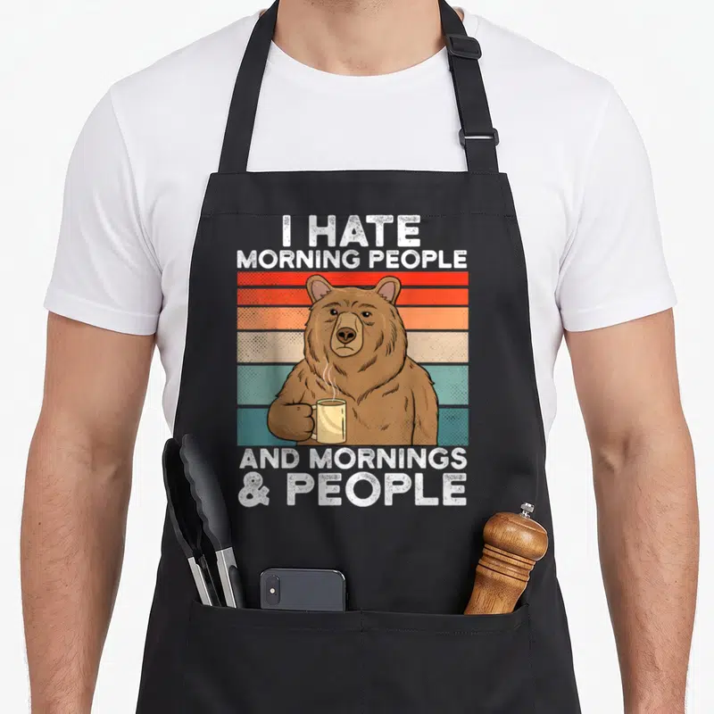 Tablier de cuisine noir avec ours tenant une tasse et texte blanc sur bandes colorées rétro.