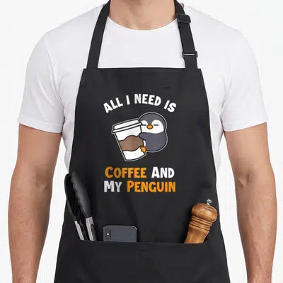 Tablier de cuisine noir avec un pingouin tenant une tasse et le texte All I Need Is Coffee And My Penguin
