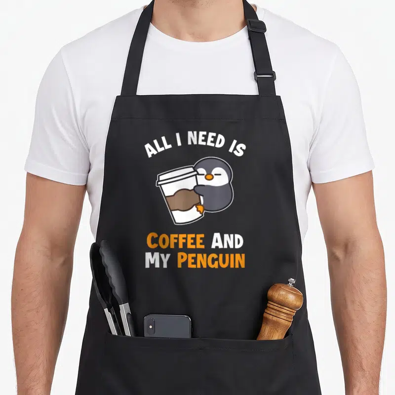 Tablier de cuisine noir avec un pingouin tenant une tasse et le texte All I Need Is Coffee And My Penguin