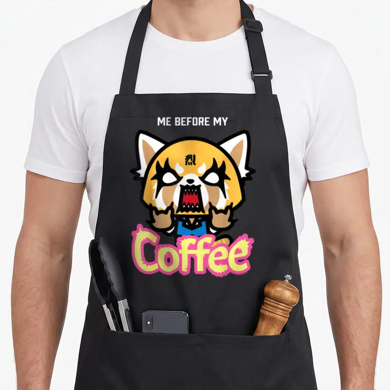 Tablier de cuisine noir avec Aggretsuko rockeuse et l'inscription Me Before My Coffee en lettres colorées.