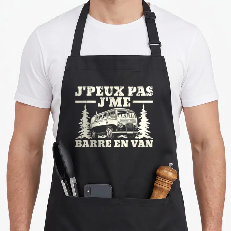 Tablier de cuisine noir avec illustration d'un van vintage blanc encadré par deux sapins et le texte J'peux pas j'me barre en van.
