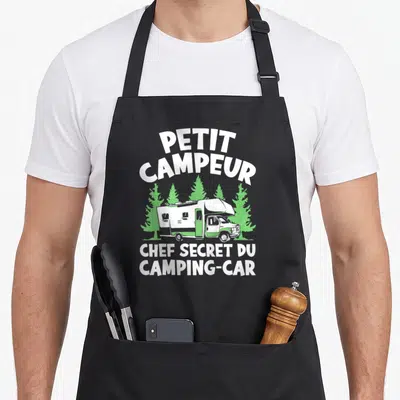 Tablier de cuisine noir avec illustration d'un camping-car blanc et vert devant des arbres verts et le texte Petit Campeur Chef Secret du Camping-Car.
