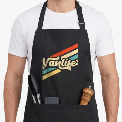 Tablier de cuisine noir avec logo Vanlife rétro et bandes colorées diagonales orange, jaune et turquoise.