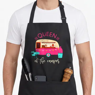 Tablier de cuisine noir avec une caravane rose et l'inscription Queen of the camper en lettres stylisées.