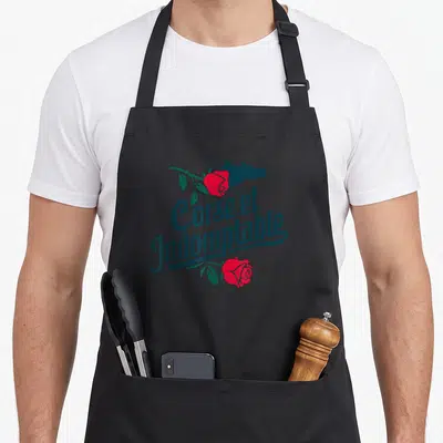 Tablier de cuisine noir avec silhouette de Corse, roses rouges et texte Corse et Indomptable Liberty en typographie stylisée.