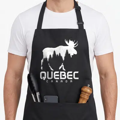 Tablier de cuisine noir avec silhouette blanche d'orignal contenant des arbres et l'inscription QUEBEC CANADA en bas.