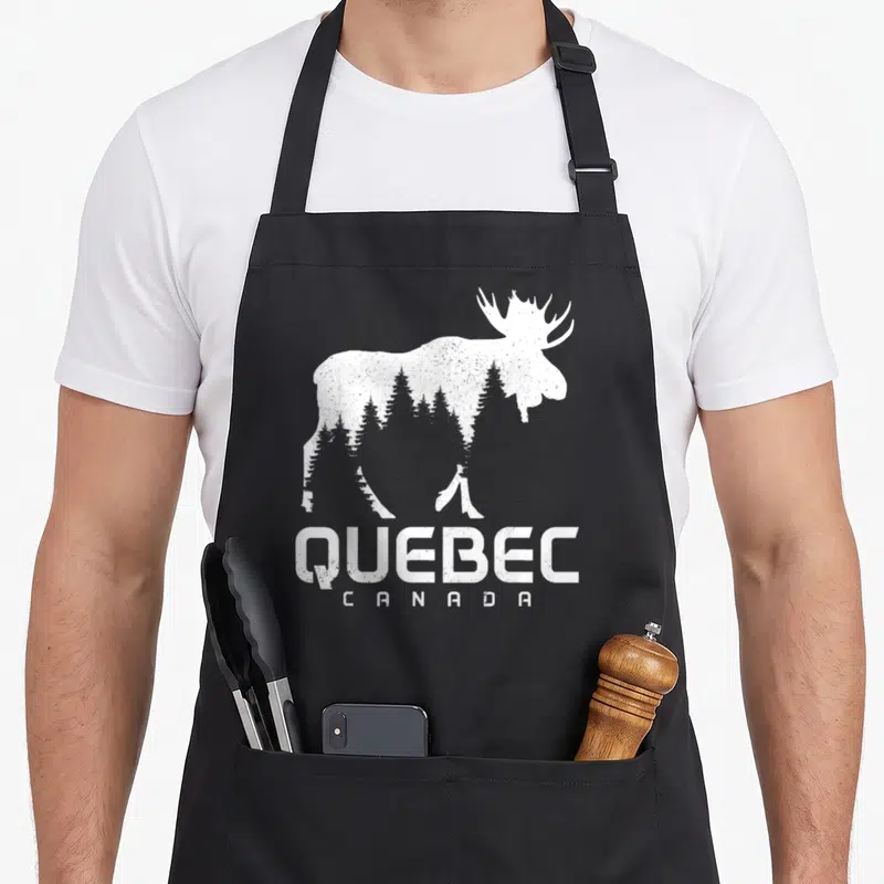 Tablier de cuisine noir avec silhouette blanche d'orignal contenant des arbres et l'inscription QUEBEC CANADA en bas.