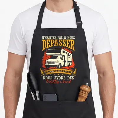 Tablier de cuisine noir avec illustration de camping-car et texte humoristique en orange et blanc.