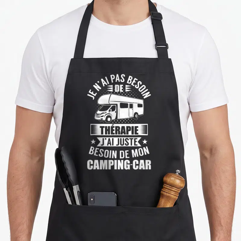 Tablier de cuisine noir avec illustration blanche d'un camping-car et texte humoristique sur fond pointillé.