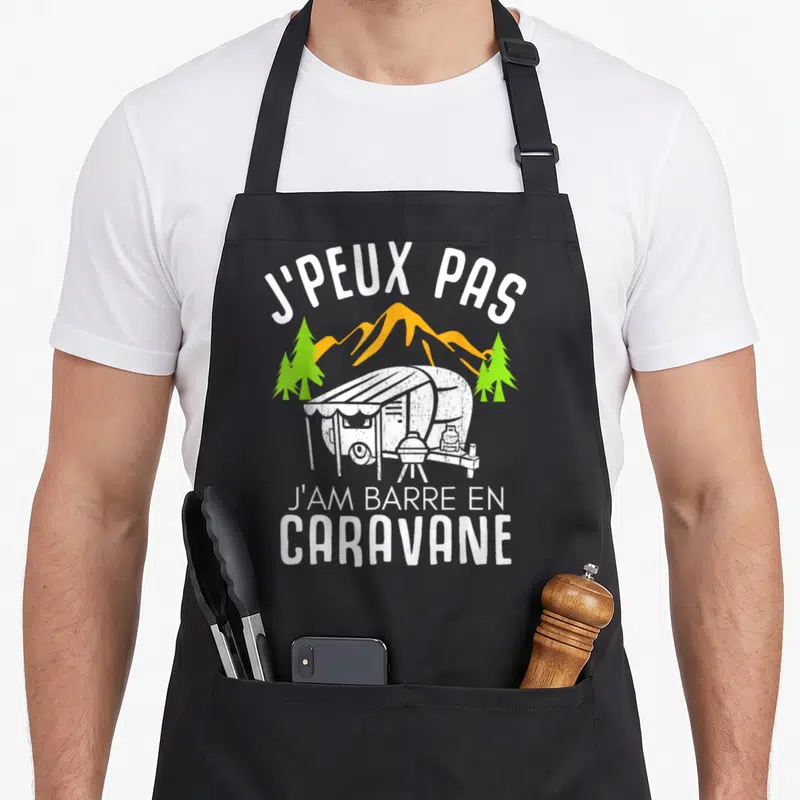Tablier de cuisine noir avec illustration de caravane, montagnes et texte humoristique sur le camping.