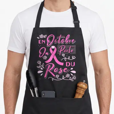 Tablier de cuisine noir avec le texte En Octobre On Porte Du Rose entouré d'un ruban rose et de motifs floraux roses
