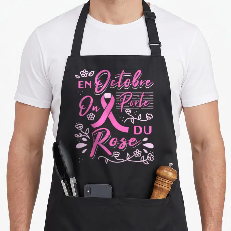 Tablier de cuisine noir avec le texte En Octobre On Porte Du Rose entouré d'un ruban rose et de motifs floraux roses