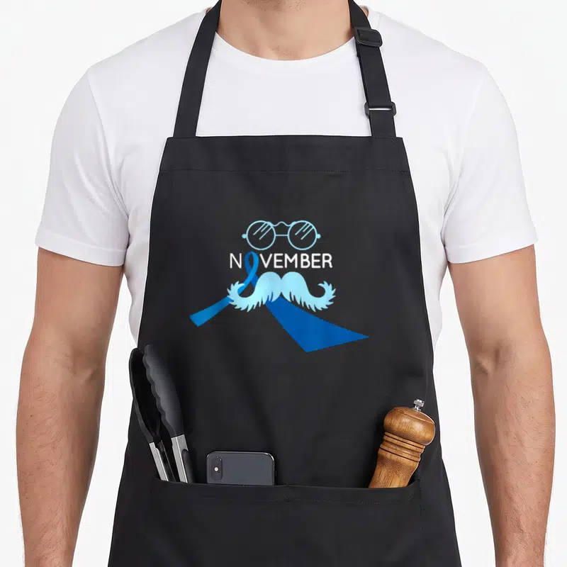 Tablier de cuisine noir avec le mot novembre, un ruban bleu, des lunettes et une moustache blanche.
