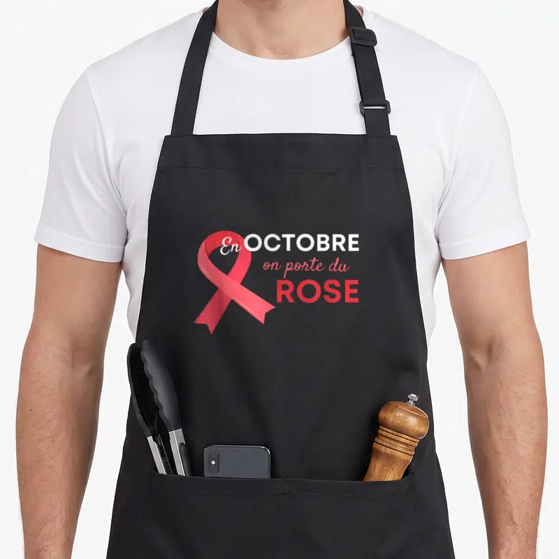 Tablier de cuisine noir avec un ruban rose et le texte En Octobre on porte du Rose imprimé au centre.